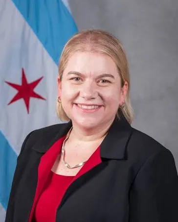 Dr. Allison Arwady in a black blazer and red top before a Chicago flag