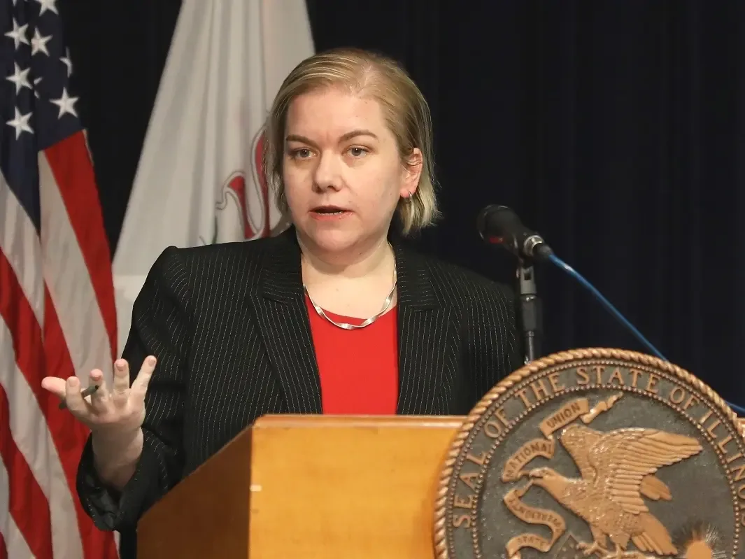 Dr. Allison Arwady speaks at a podium bearing the State of Illinois seal, flags behind her