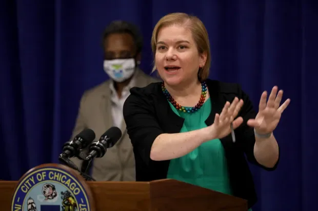 Dr. Allison Arwady gestures at a City of Chicago podium, Mayor Lori Lightfoot behind her