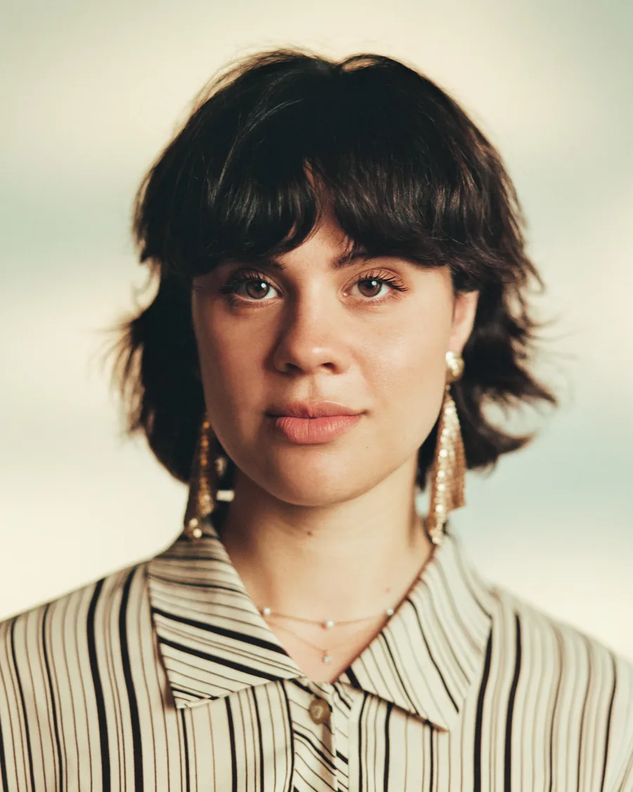 Anna Garcia in a striped collared shirt and long earrings looks directly at the camera