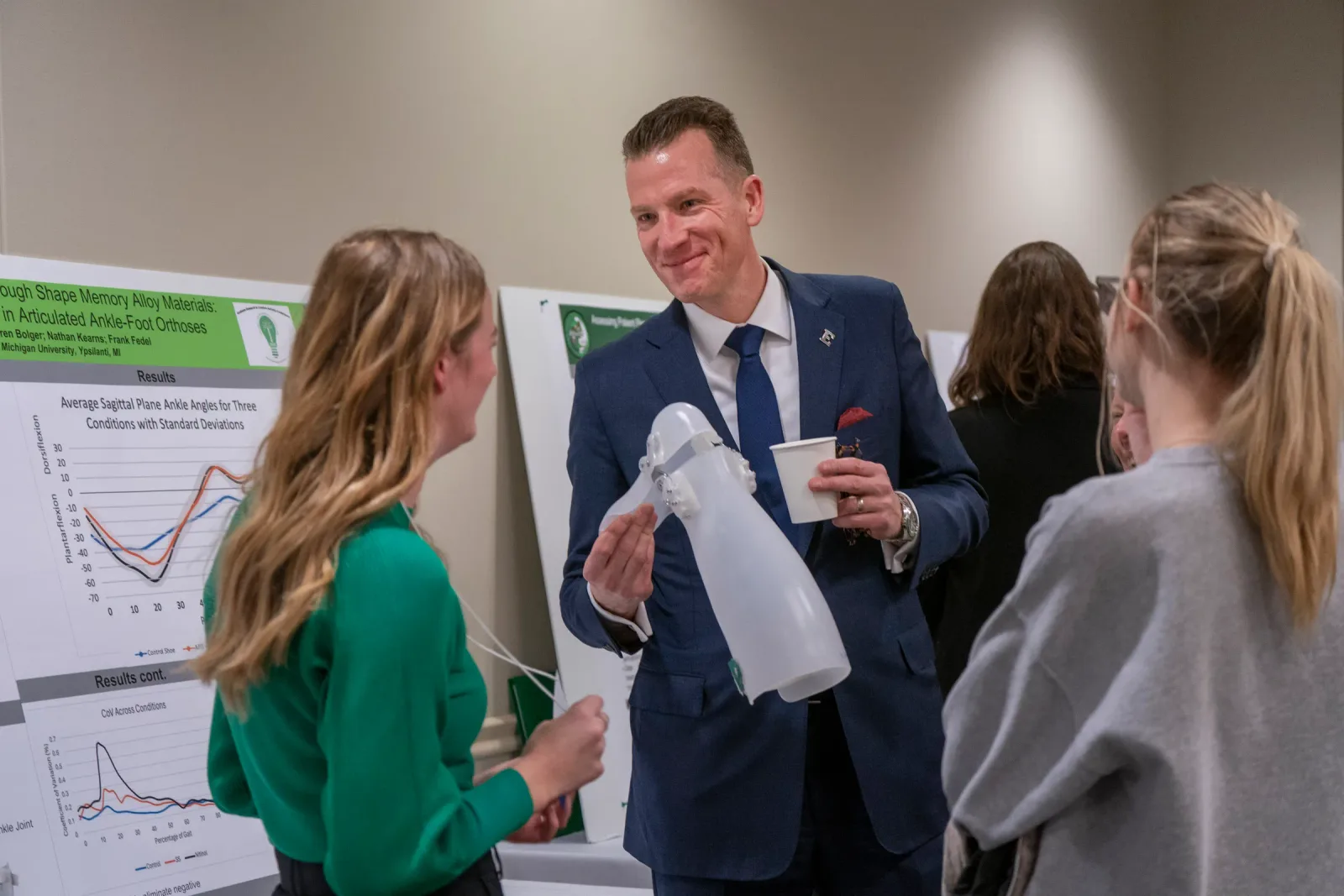 Brendan Kelly holds an orthotic device and a coffee cup while talking with students at research posters