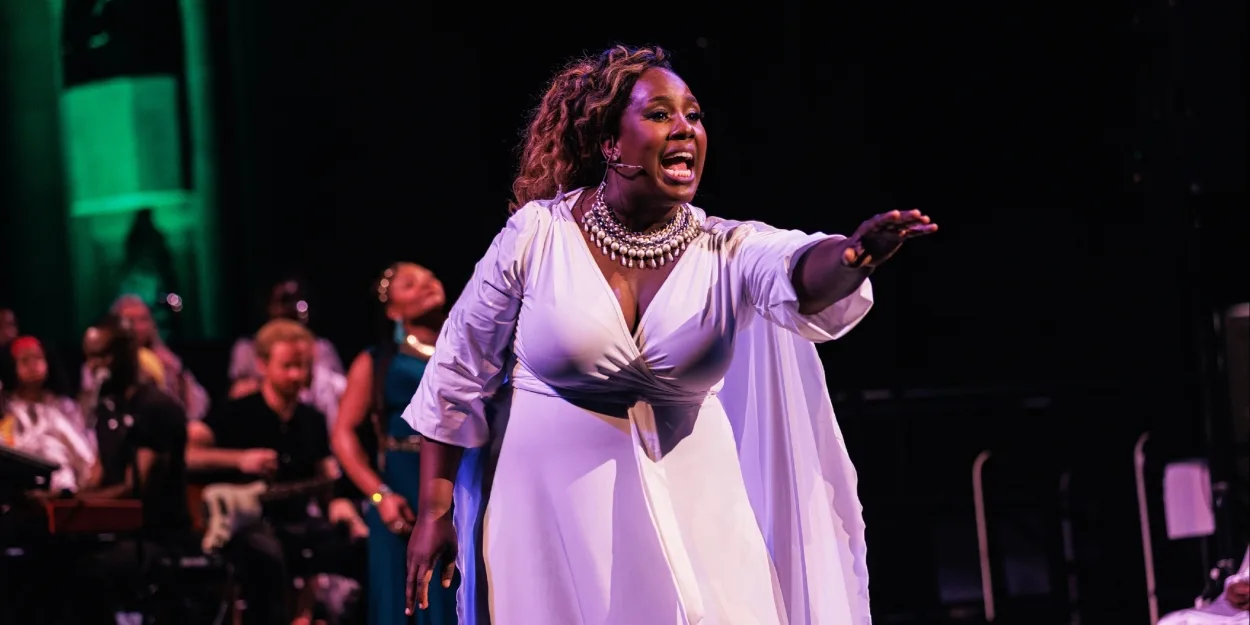 Crystal Lucas-Perry singing on stage in a white gown, arm extended, green stage light behind her