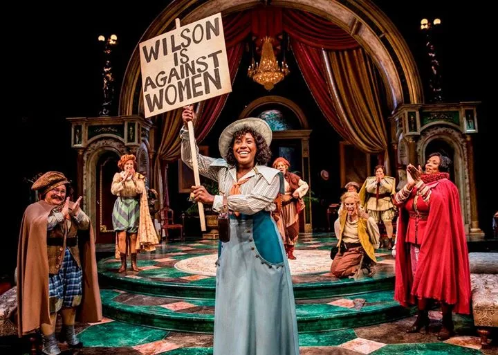 Crystal Lucas-Perry as John Adams holding a Wilson Is Against Women protest sign in a production of 1776