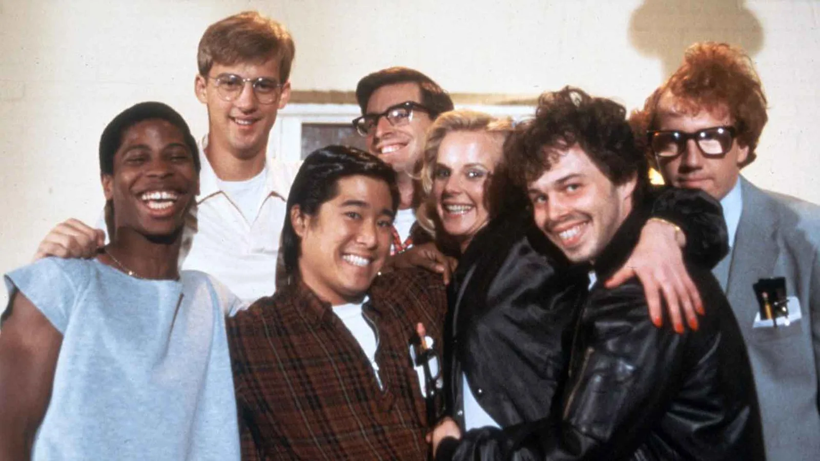 Seven cast members of Revenge of the Nerds crowded together and smiling in a publicity photo