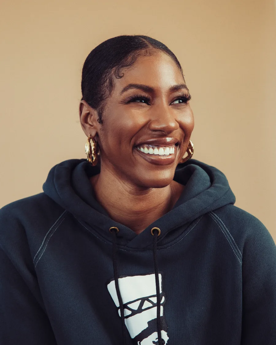 Diarra Kilpatrick smiling in a dark hoodie and gold hoop earrings