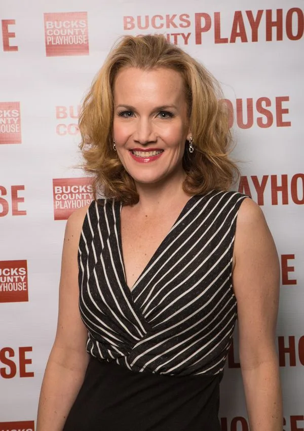 Erin Dilly smiles in a striped dress in front of a Bucks County Playhouse backdrop