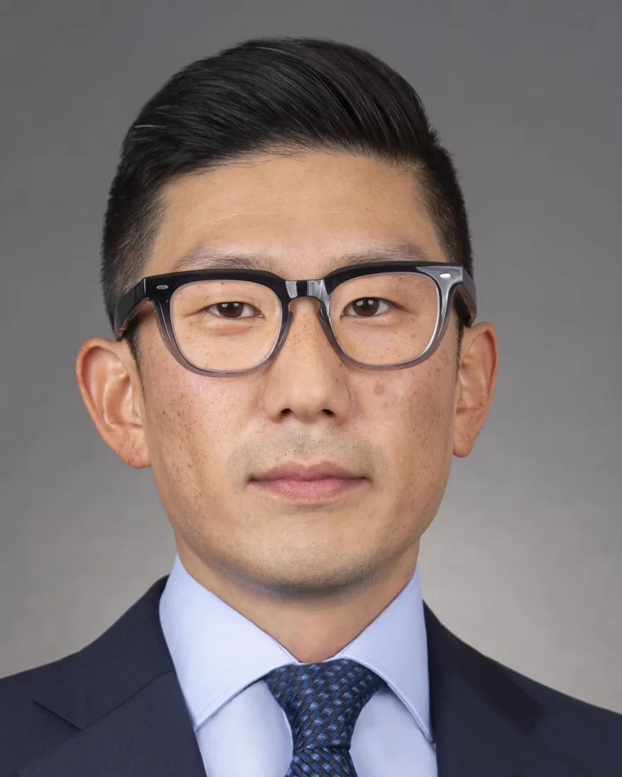 Eugene Kang in a dark suit and glasses against a grey studio background