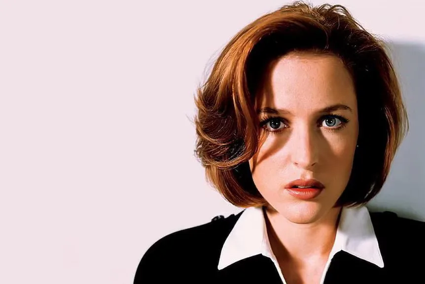 Gillian Anderson, red hair styled in a bob, wearing a black top with a white collar