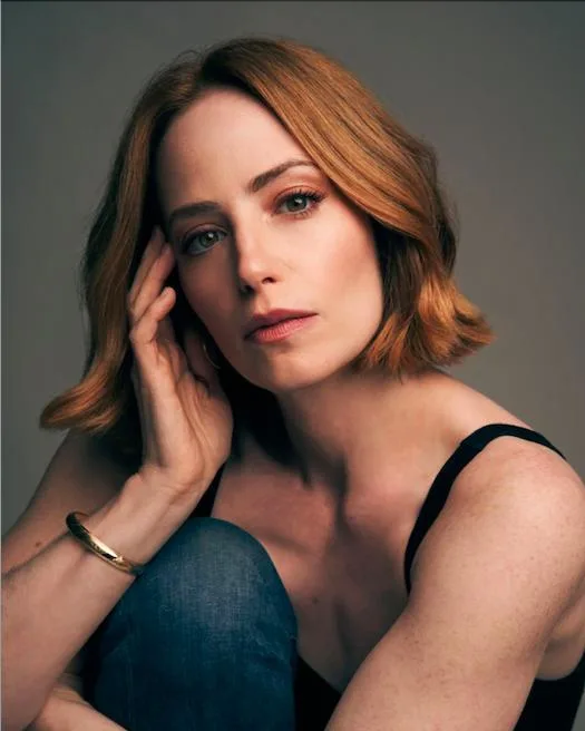 Jaime Ray Newman smiling in a portrait, dark red hair falling past her shoulders