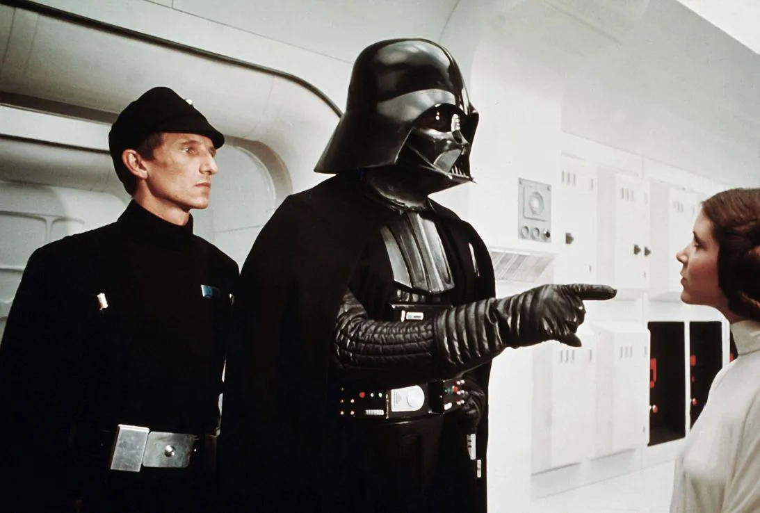 Darth Vader points at Princess Leia beside an Imperial officer aboard a ship