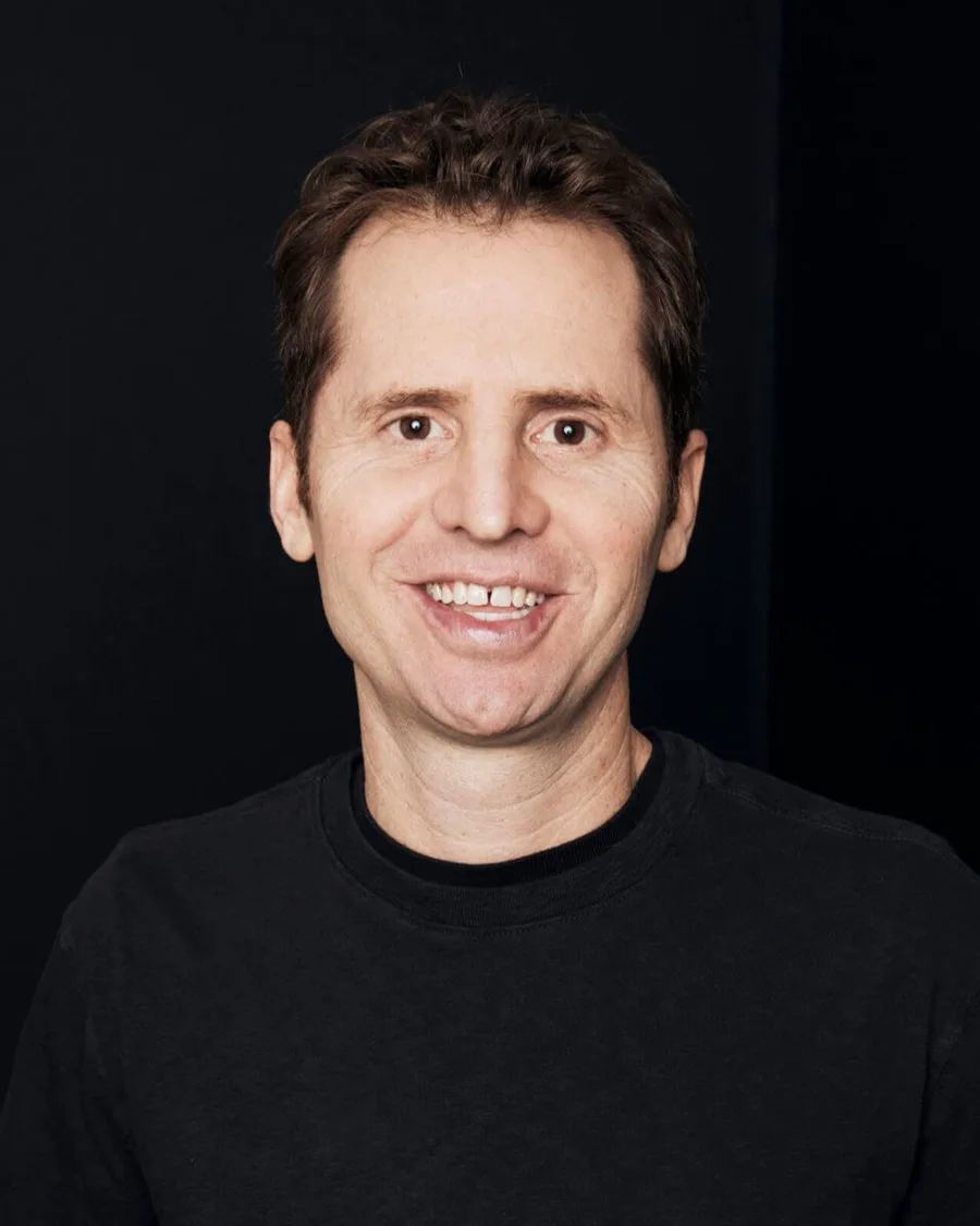 Jeff Clune in a black t-shirt smiles broadly against a dark background