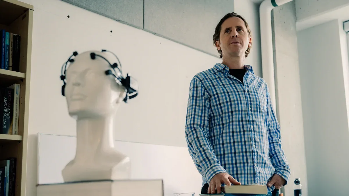 Jeff Clune stands with books beside a mannequin head wearing an EEG headset