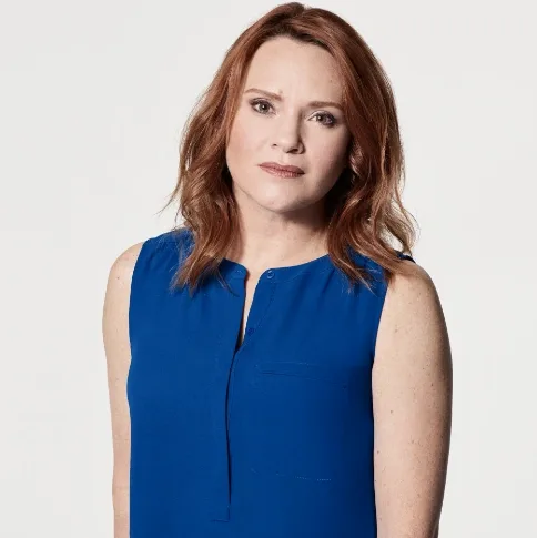 Jennifer Laura Thompson with red hair in a blue sleeveless top against a plain light background