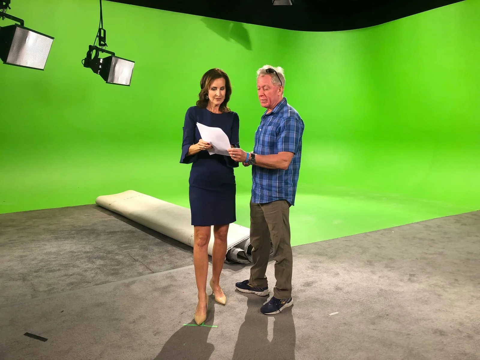 JoAnne Purtan in a navy dress reviews a script with a man on a green-screen studio set