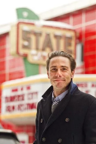Joseph Beyer smiles in a dark peacoat outside the State Theatre, its marquee behind him