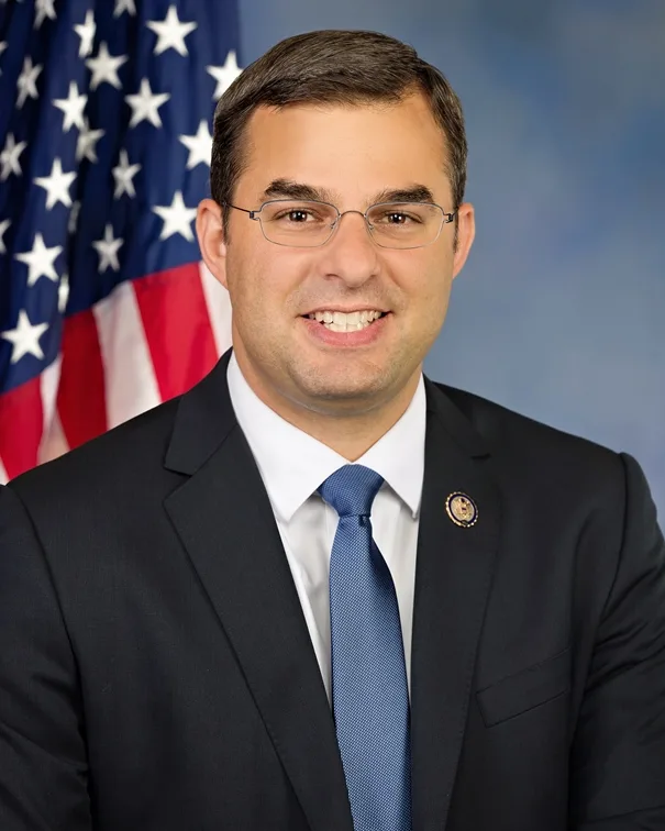 Official portrait of Justin Amash in a dark suit and blue tie before an American flag