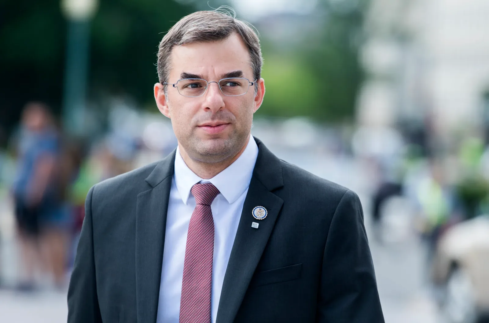 Justin Amash in a dark suit and red tie photographed outdoors on a blurred street