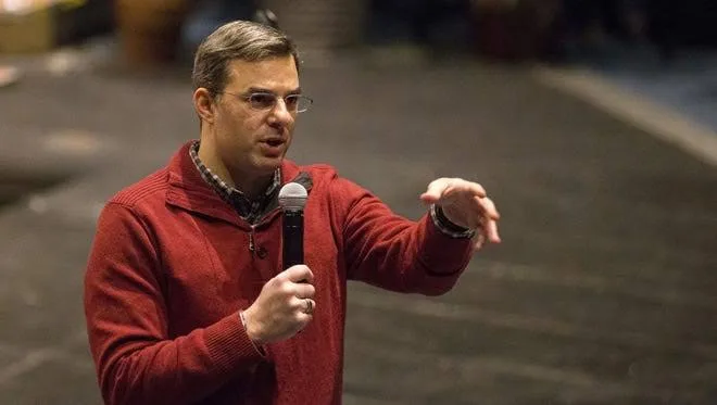 Justin Amash in a red sweater gestures while speaking into a handheld microphone