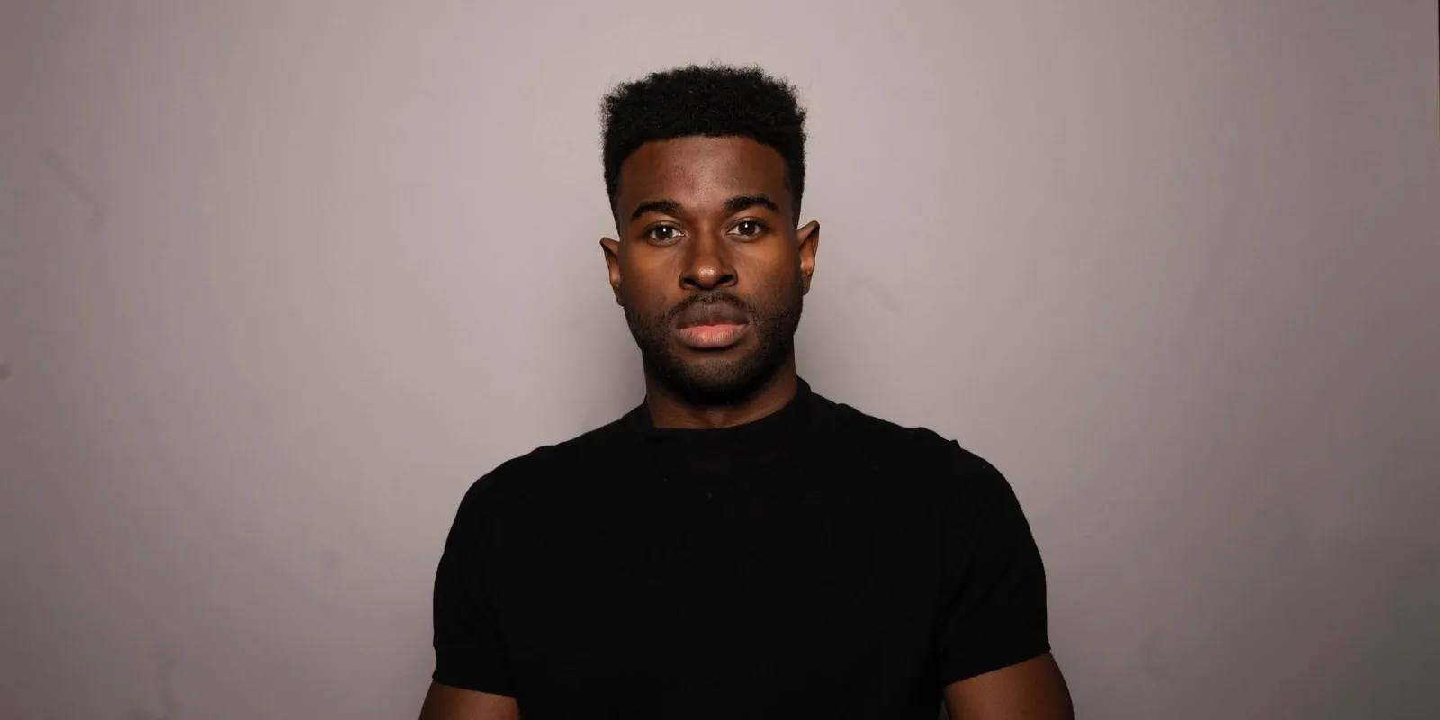 Lee Alexander in a black t-shirt faces the camera against a plain grey studio backdrop