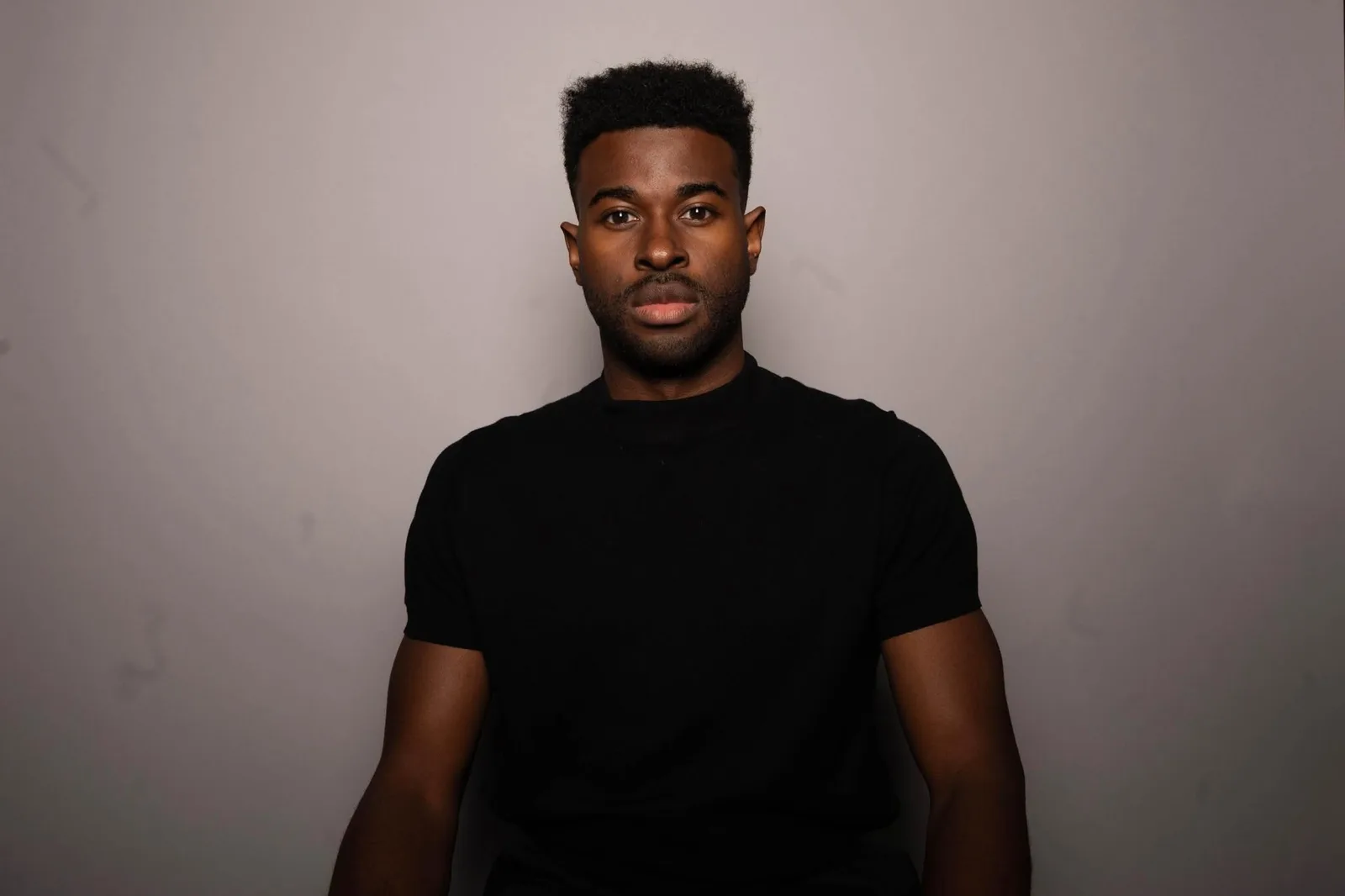 Lee Alexander in a black t-shirt faces the camera against a plain grey studio backdrop