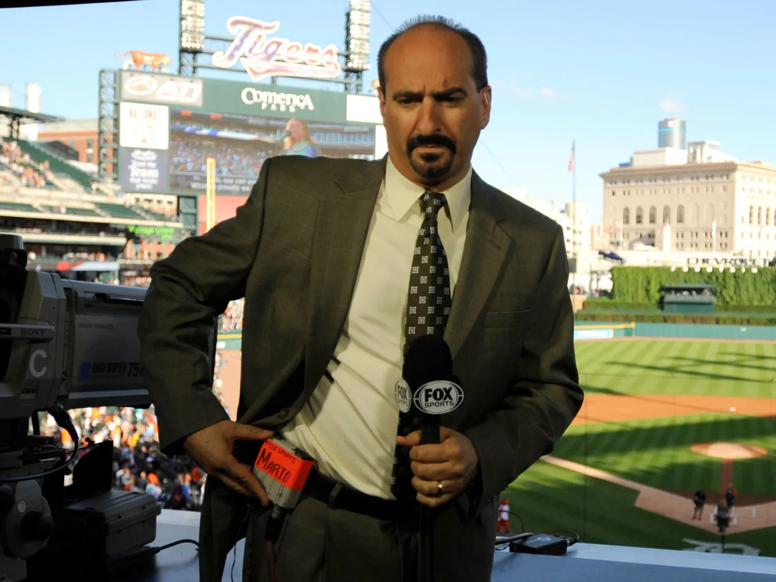 Mario Impemba adjusting a microphone pack in the broadcast booth at Comerica Park