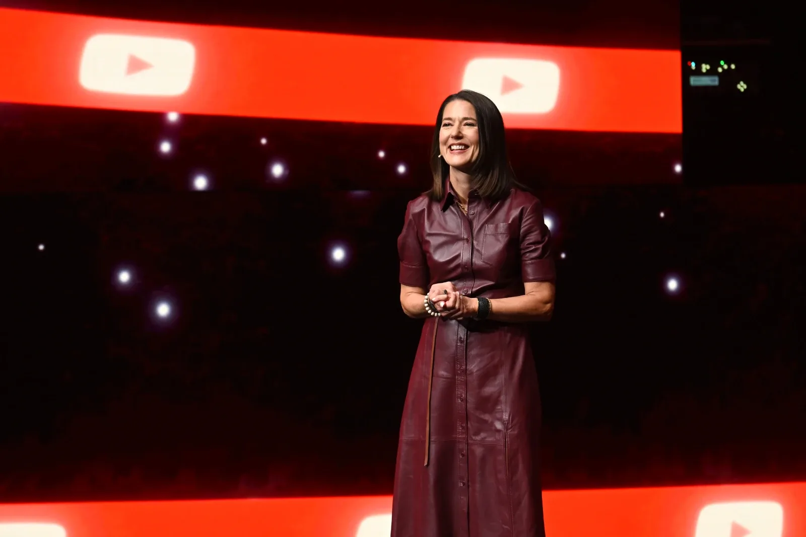 Mary Ellen Coe speaking on stage in a burgundy leather dress in front of YouTube branding