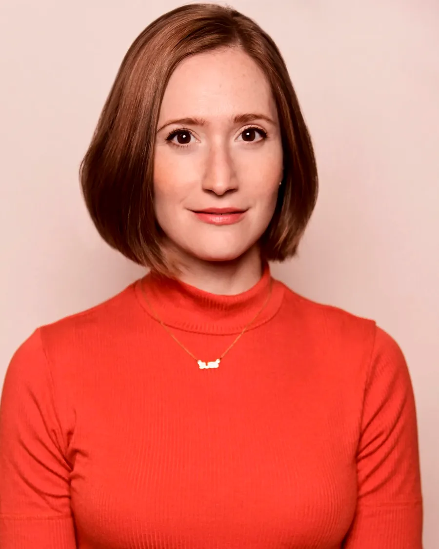 Studio portrait of Rachel Sussman in an orange mock-neck top against a pale background