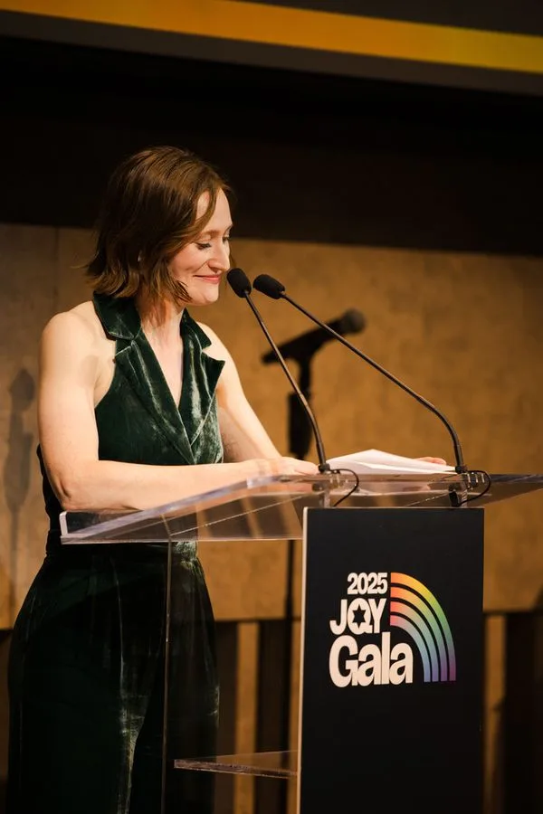 Rachel Sussman speaks from a clear lectern with microphones at the JQY Gala