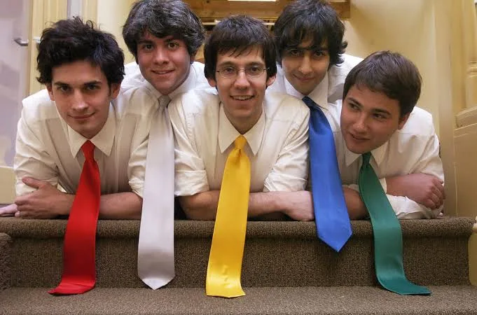 Five young men in white shirts and coloured ties lean over a carpeted staircase