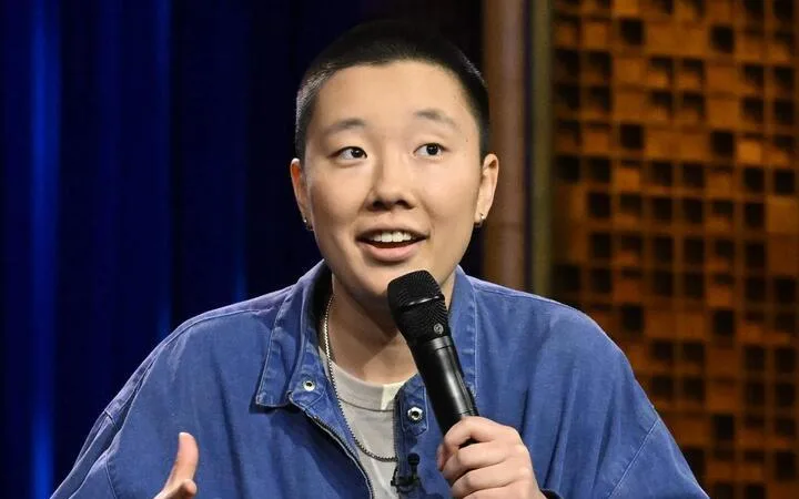 Sabrina Wu speaking into a handheld microphone in front of a blue curtain and brick wall