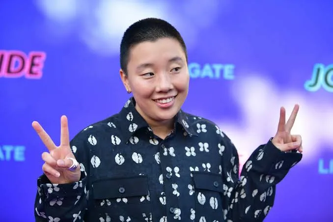 Sabrina Wu smiling and making peace signs in a patterned shirt before a purple premiere backdrop