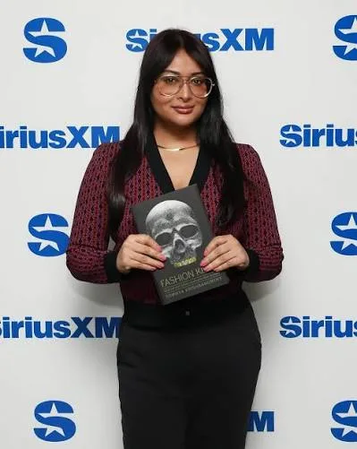 Sowmya Krishnamurthy holding a copy of her book Fashion Killa in front of a SiriusXM backdrop