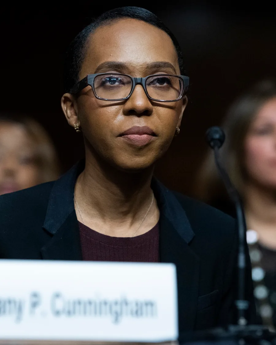 Tiffany P. Cunningham in a dark blazer at a hearing table, a nameplate bearing her name in front of her