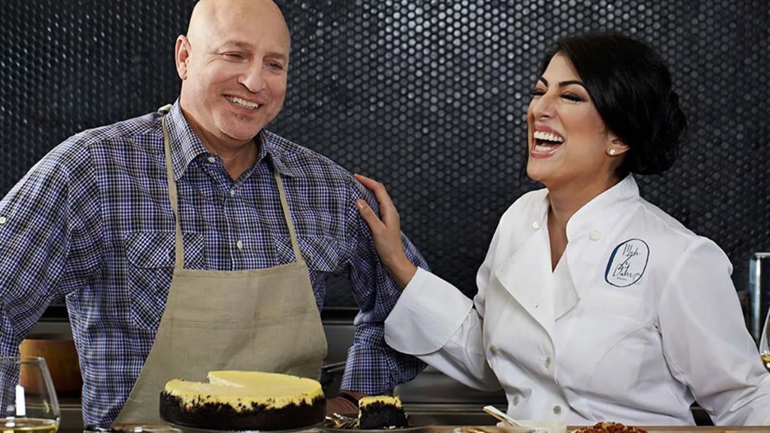 Umber Ahmad smiling alongside chef Tom Colicchio next to a cheesecake