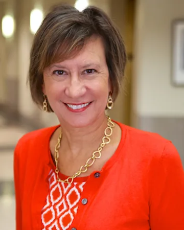 Valorie Vojdik smiling in a faculty portrait, wearing a red-orange cardigan and a gold chain necklace