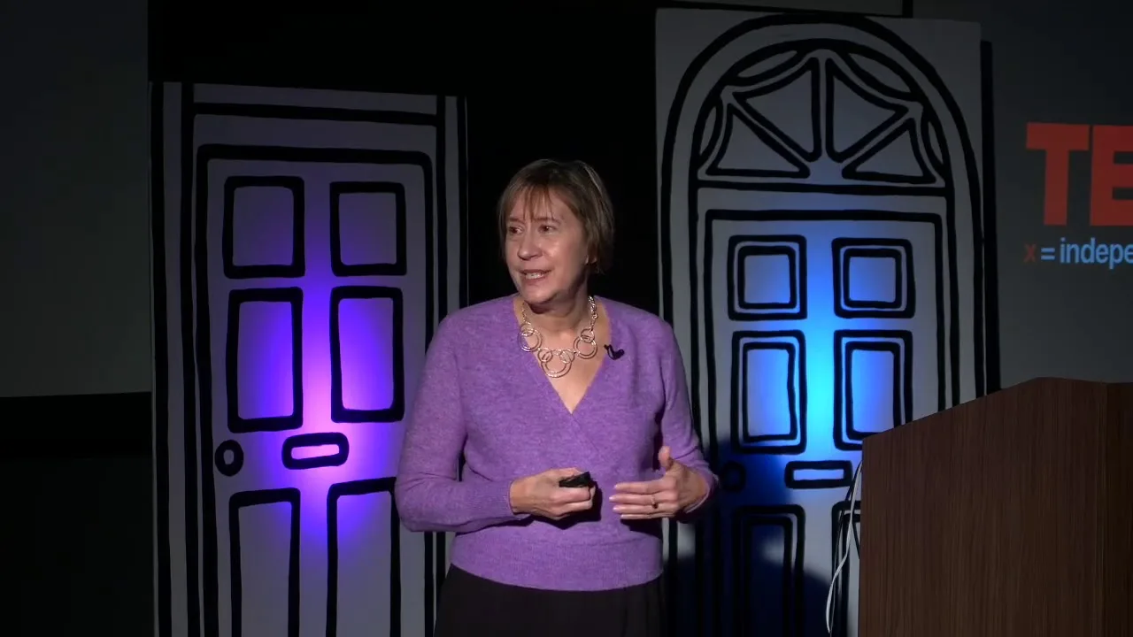 Valorie Vojdik speaking on the TEDxUTK stage in a lavender sweater, with illustrated doors behind her
